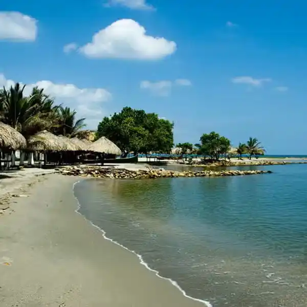 Playa La Ciénaga en Coveñas con aguas tranquilas, arena clara y palapas frente al mar Caribe.