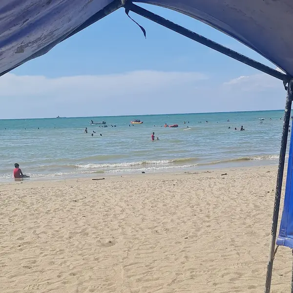 Personas disfrutando de la playa en la Primera Ensenada de Coveñas, vista desde la sombra de una carpa.